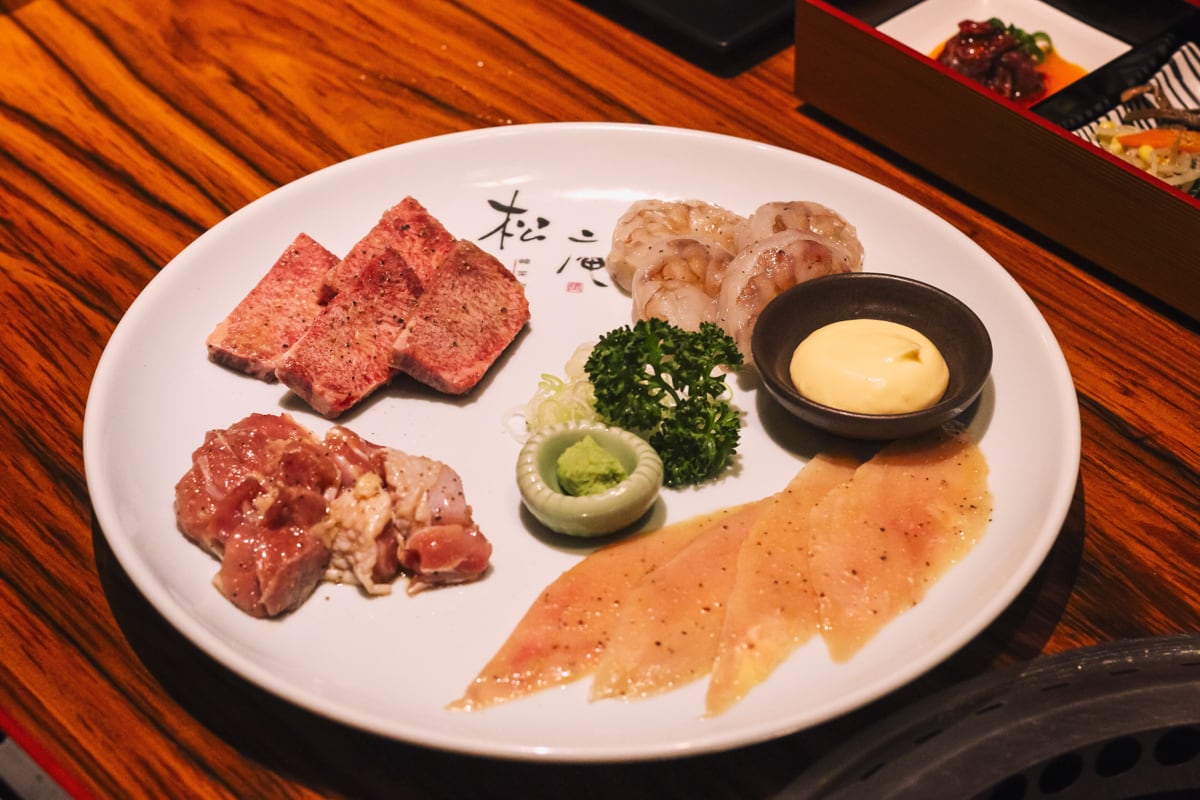 大皿に四種類の具材が並び、中央にネギ・パセリ・ワサビ、右側にマヨネーズが置いてある。時計回り上から、天然ぶつ切り大エビ・・塩ミノ・名古屋コーチン・厚切り上塩タン