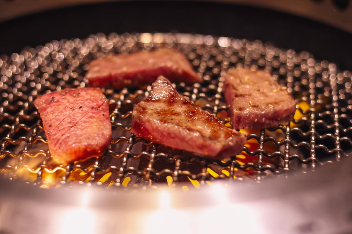 焼き肉の網の上に4切れのタンが並んでいる様子、中央のタンはちょうど良い焼き具合