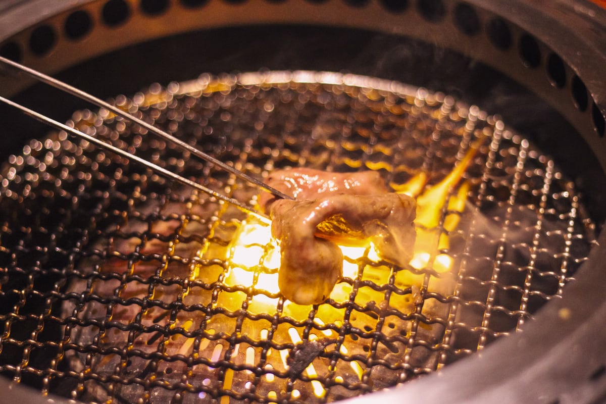 網の上で色が変わり始めた肉をトングで折りたたんでいく様子