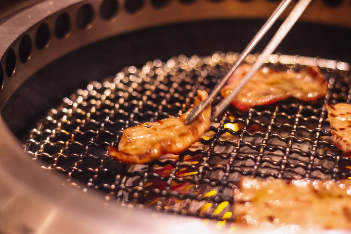 網の上にある肉をトングで掴んでいる様子