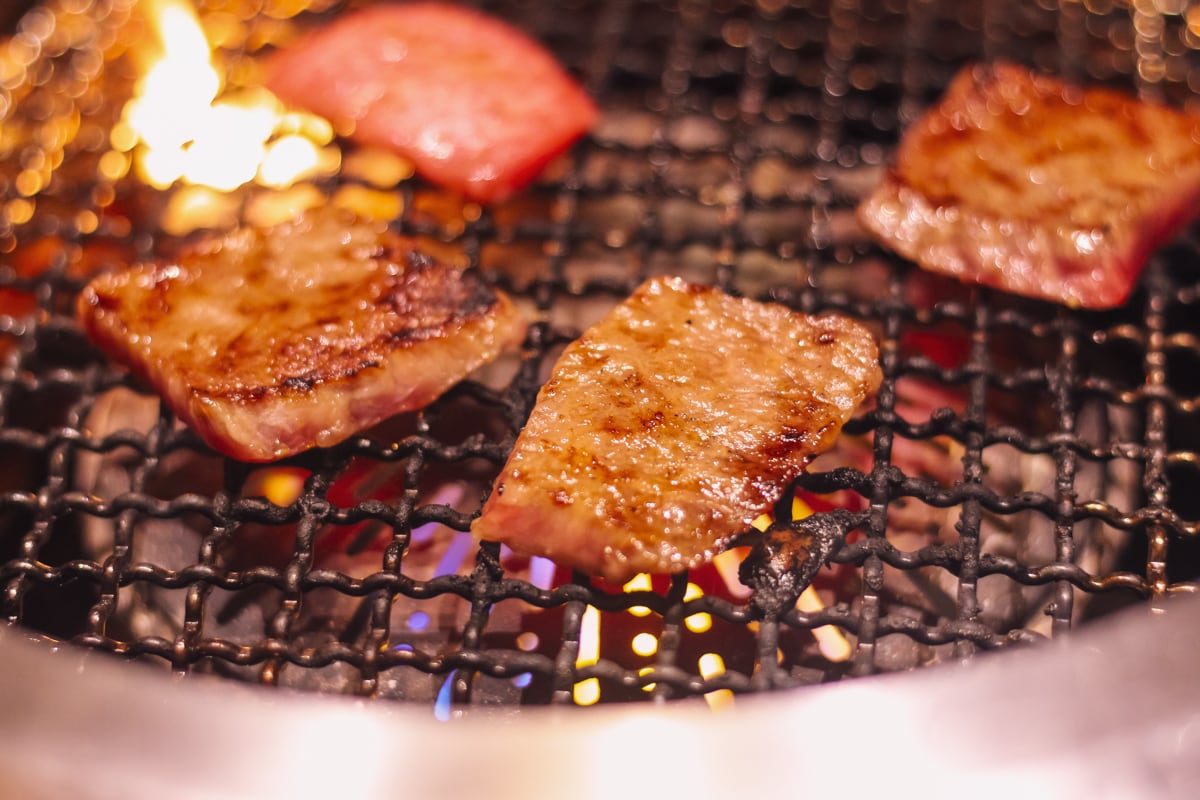 網の上に4切れの肉、手前はちょうど良い焼き具合。左奥で炎が上がっている