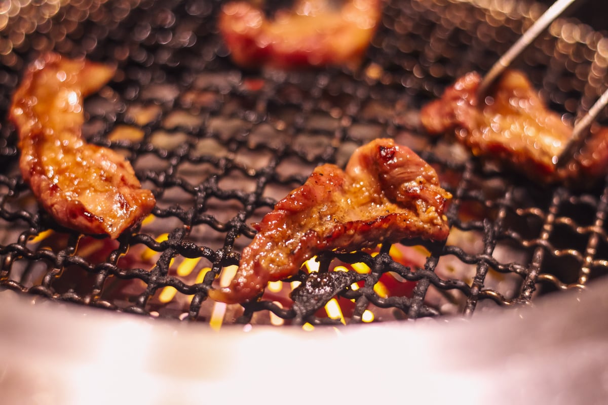 網の上に4切れの肉、焼くと縮むため右側の肉をトングで抑えている