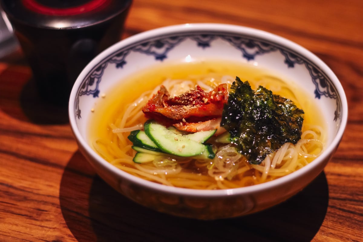 白い器に琥珀色のスープ、麺のうえにキムチ・きゅうり・海苔・ごまがトッピングされている