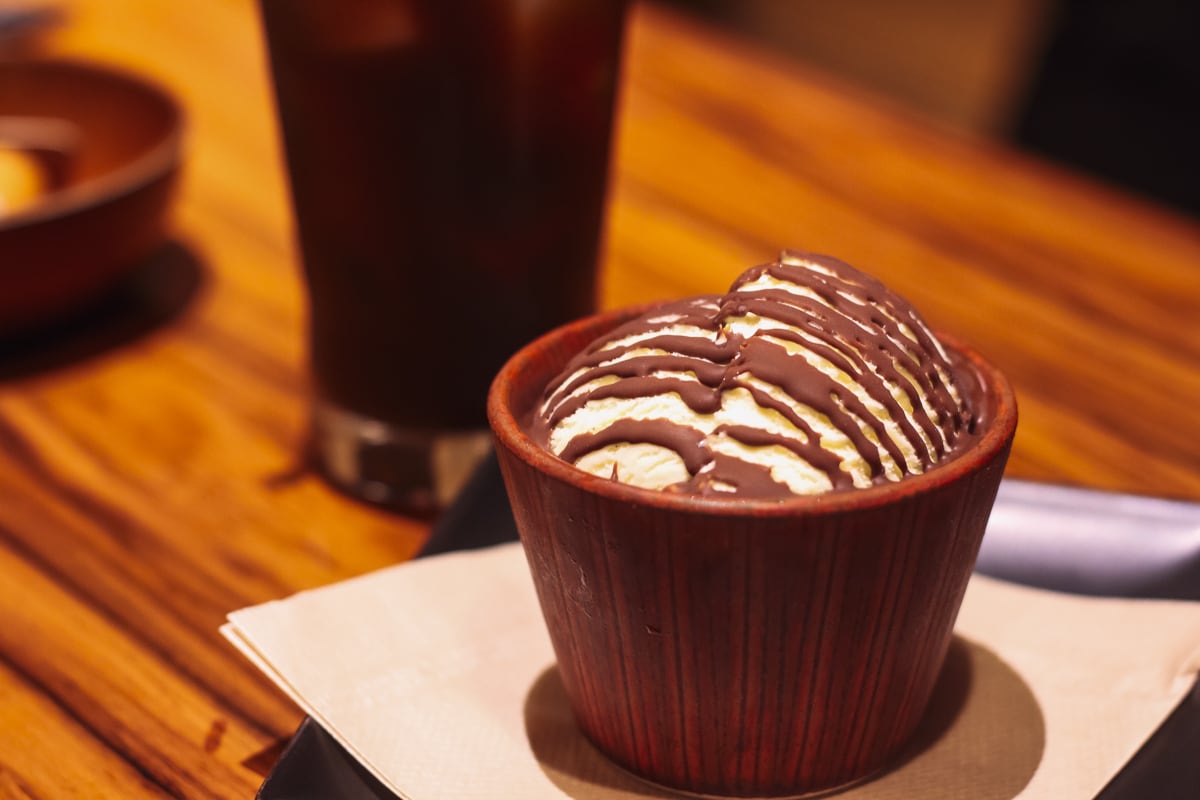 木目調の器にアイスが盛られ、チョコレートソースがかかっている