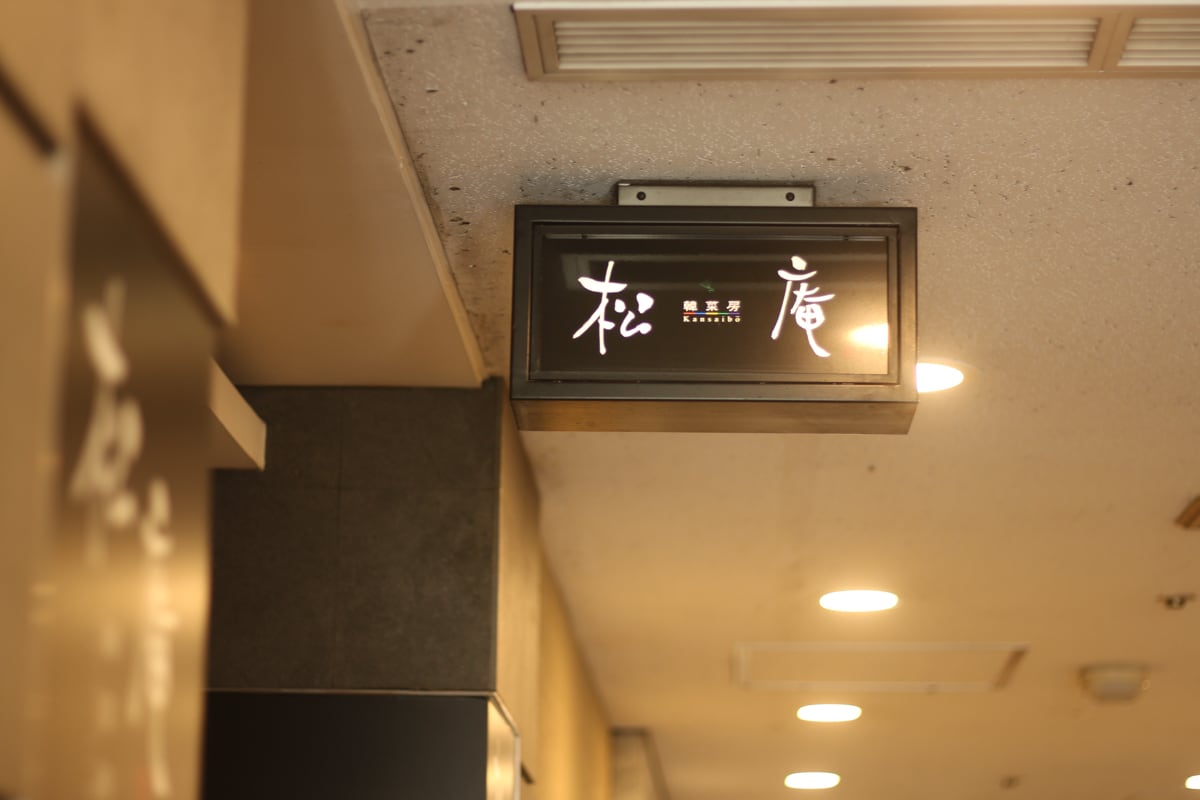 天井から吊り下げられた形で設置されているお店の看板。黒い長方形の箱に「松庵」と書かれている